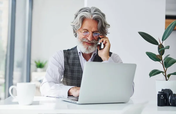 Boss in formal clothes works in office. Senior stylish modern man with grey hair and beard indoors.
