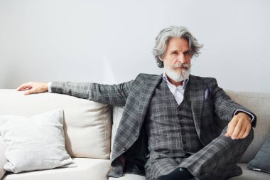 Resmi kıyafetlerle rahat koltukta oturuyor. Gri saçlı ve sakallı son sınıf modacı modern adam..
