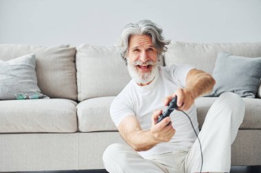 Denetleyici kullanarak video oyunu oynar. Gri saçlı ve sakallı son sınıf modacı modern adam..