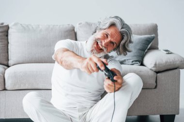 Denetleyici kullanarak video oyunu oynar. Gri saçlı ve sakallı son sınıf modacı modern adam..