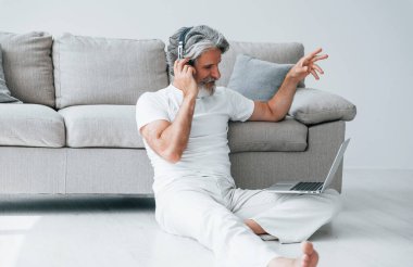 Dizüstü bilgisayarla kanepede oturur ve müzik dinler. Gri saçlı ve sakallı son sınıf modacı modern adam..