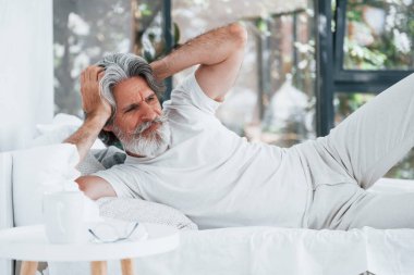 Hasta, son sınıf modası geçmiş, gri saçlı, sakallı, yatakta yatan ve kendini kötü hisseden modern bir adam..