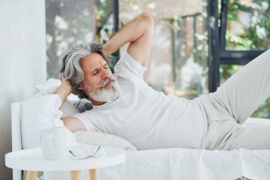 Hasta, son sınıf modası geçmiş, gri saçlı, sakallı, yatakta yatan ve kendini kötü hisseden modern bir adam..