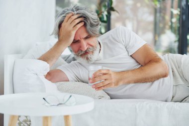 Hasta, son sınıf modası geçmiş, gri saçlı, sakallı, yatakta yatan ve kendini kötü hisseden modern bir adam..