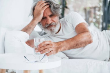 Hasta, son sınıf modası geçmiş, gri saçlı, sakallı, yatakta yatan ve kendini kötü hisseden modern bir adam..