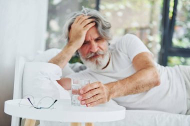 Hasta, son sınıf modası geçmiş, gri saçlı, sakallı, yatakta yatan ve kendini kötü hisseden modern bir adam..