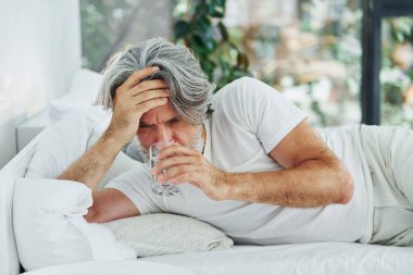 Hasta, son sınıf modası geçmiş, gri saçlı, sakallı, yatakta yatan ve kendini kötü hisseden modern bir adam..