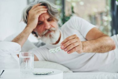 Hasta, son sınıf modası geçmiş, gri saçlı, sakallı, yatakta yatan ve kendini kötü hisseden modern bir adam..