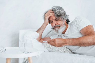 Hasta, son sınıf modası geçmiş, gri saçlı, sakallı, yatakta yatan ve kendini kötü hisseden modern bir adam..