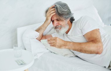 Hasta, son sınıf modası geçmiş, gri saçlı, sakallı, yatakta yatan ve kendini kötü hisseden modern bir adam..