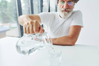 Bardağa su döker. Gri saçlı ve sakallı son sınıf modacı modern adam..