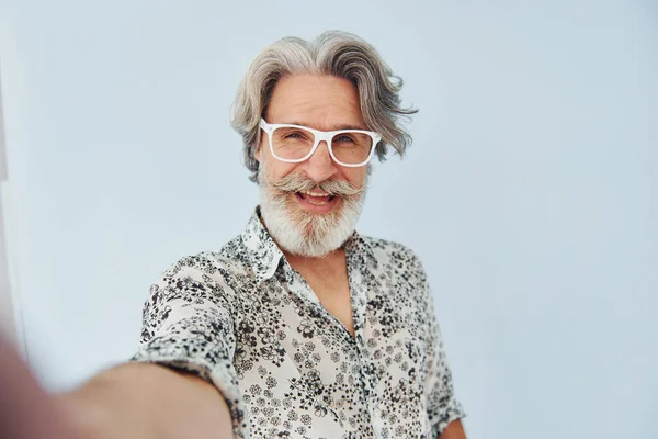 Tourist makes selfie. Senior stylish modern man with grey hair and beard indoors.