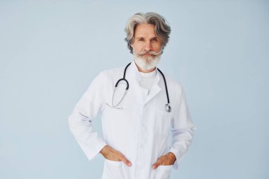 Duvara yaslanmış beyaz önlüklü doktor. Gri saçlı ve sakallı son sınıf modacı modern adam..