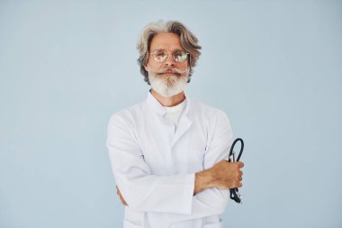Duvara yaslanmış beyaz önlüklü doktor. Gri saçlı ve sakallı son sınıf modacı modern adam..