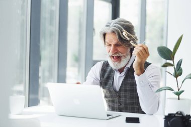 İş adamı dizüstü bilgisayarla masaya oturur. Gri saçlı ve sakallı son sınıf modacı modern adam..