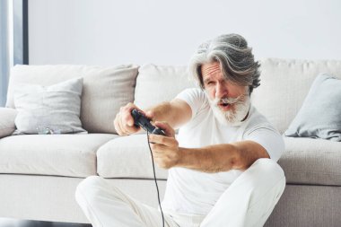 Denetleyici kullanarak video oyunu oynar. Gri saçlı ve sakallı son sınıf modacı modern adam..