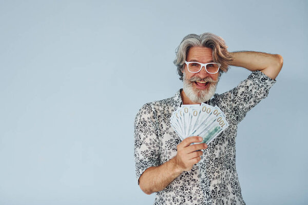 Millionaire with cash in hands. Senior stylish modern man with grey hair and beard indoors.