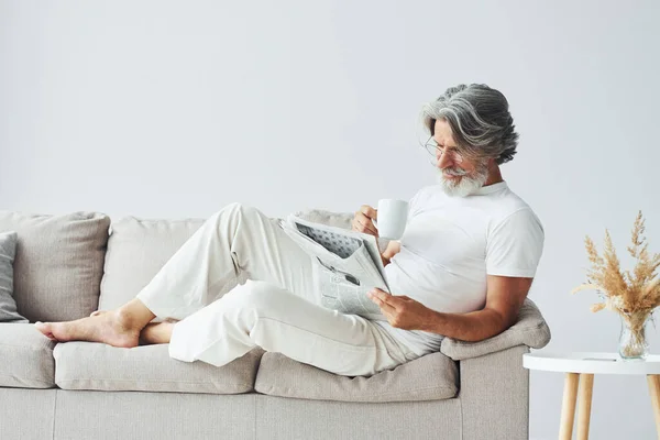 Having a rest on the sofa. Senior stylish modern man with grey hair and beard indoors.