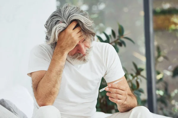 Conception of illness and virus. Senior stylish modern man with grey hair and beard indoors.