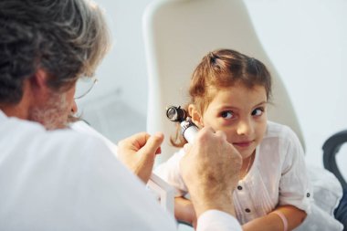 Küçük kızın ziyareti var. Beyaz önlüklü, gri saçlı ve sakallı kıdemli otorhinolarygolog klinikte..