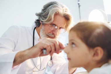 Küçük kızın ziyareti var. Beyaz önlüklü, gri saçlı ve sakallı kıdemli otorhinolarygolog klinikte..
