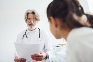 Küçük kıza yapılan muayenenin sonuçlarını okuyorum. Beyaz önlüklü, gri saçlı ve sakallı kıdemli erkek doktor klinikte..