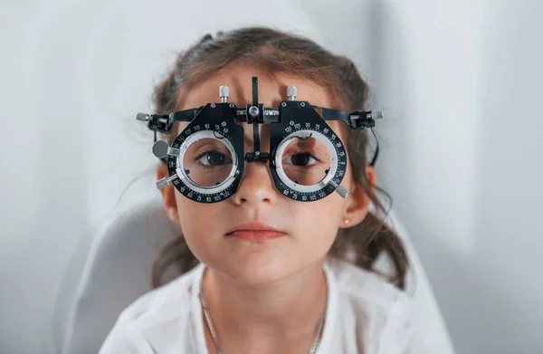 Cute little girl is in ophthalmology clinic with special tool on eyes getting tested.