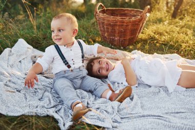 Şirin erkek ve kız kardeşler dışarıda oynuyorlar. Arka planda güzel ağaçlar ve güneş ışığı var..