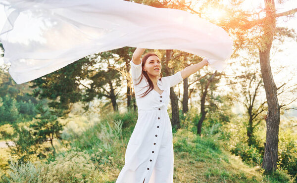 Happy young woman dancing with white cloth in hands outdoors in the forest.