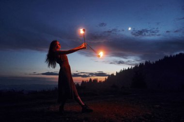 Kadın sahne sanatçısı, gece karanlığında yangın sırasında yanan sopa çeviriyor.