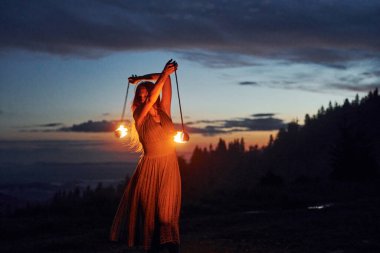 Kadın sahne sanatçısı, gece karanlığında yangın sırasında yanan sopa çeviriyor.