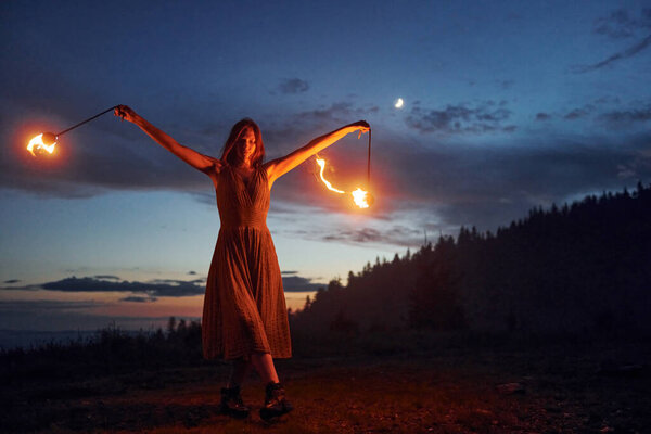 Woman performer twirl burning baton during fire performance in dark night outdoors
