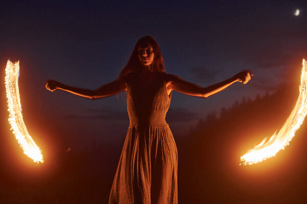 Woman performer twirl burning baton during fire performance in dark night outdoors