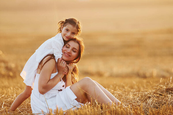 Happy mother with her little daughter spending time together outdoors on the field.