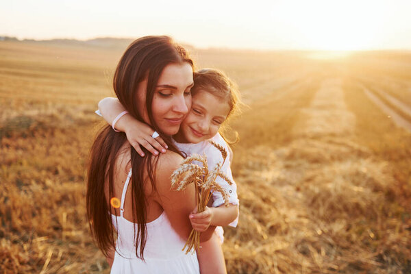 Positive little girl with her mother have weekend outdoors on the summer field together.