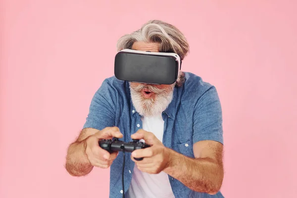 玩虚拟现实眼镜和操纵杆游戏 时髦的现代老人 灰白的头发和胡子在室内 — 图库照片