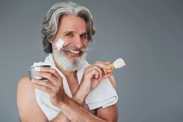 With shaving gel. Stylish modern senior man with gray hair and beard is indoors.