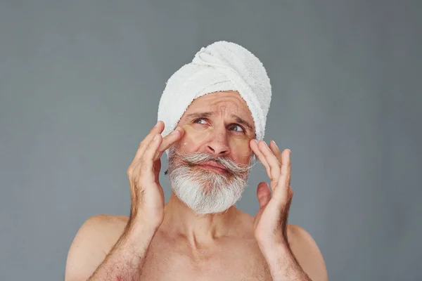 With white towel on head. Stylish modern senior man with gray hair and beard is indoors.