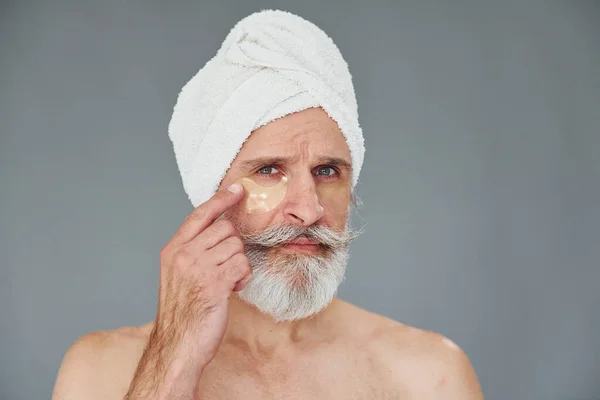 With white towel on head. Stylish modern senior man with gray hair and beard is indoors.