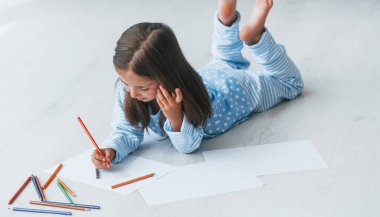 Yerde yatıp çizim yapmak. Evde yalnız başına sevimli küçük bir kız..