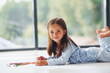 Yerde yatıp çizim yapmak. Evde yalnız başına sevimli küçük bir kız..