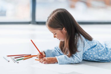 Yerde yatıp çizim yapmak. Evde yalnız başına sevimli küçük bir kız..