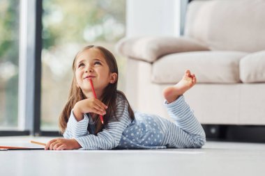 Yerde yatıp çizim yapmak. Evde yalnız başına sevimli küçük bir kız..