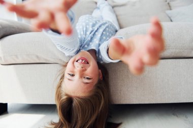 Kanepede baş aşağı yatıyordu. Evde yalnız başına sevimli küçük bir kız. Çocuk hafta sonu eğleniyor.