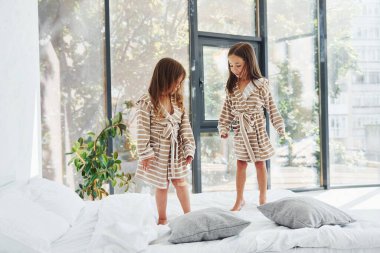 Yatağa atlamak. Evde birlikte oturan iki küçük tatlı kız. Çocuklar eğleniyor..