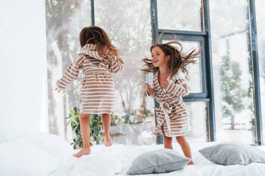 Yatağa atlamak. Evde birlikte oturan iki küçük tatlı kız. Çocuklar eğleniyor..