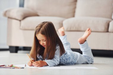 Yerde yatıp çizim yapmak. Evde yalnız başına sevimli küçük bir kız..