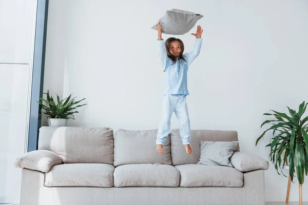Jumping on the sofa. Cute little girl indoors at home alone. Child enjoying weekend.