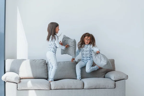 Pillow fight. Two cute little girls indoors at home together. Children having fun.