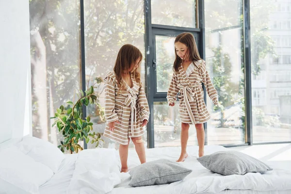 Yatağa atlamak. Evde birlikte oturan iki küçük tatlı kız. Çocuklar eğleniyor..